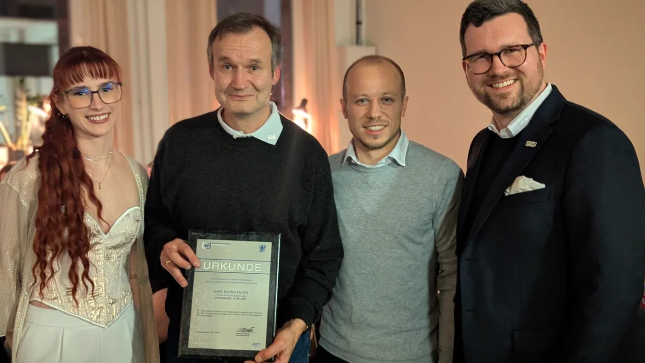 Vier Personen bei einer Abendveranstaltung, eine gerahmte Urkunde wird in die Kamera gehalten.