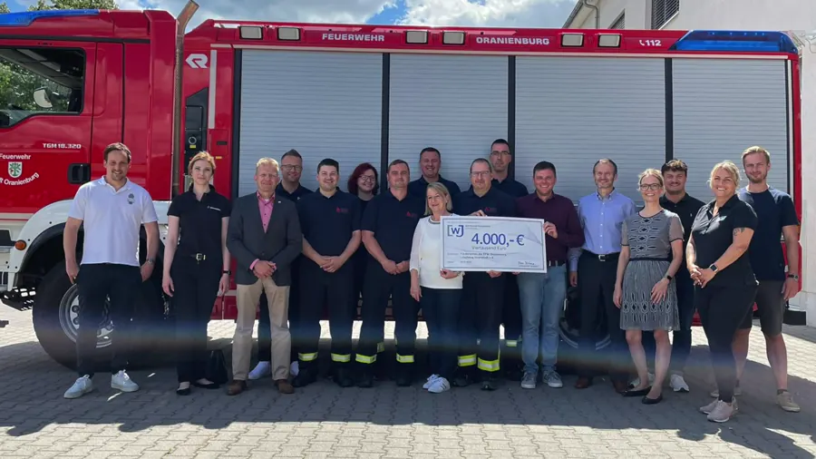 Gruppe vor einem Feuerwehrfahrzeug in Oranienburg, in der Mitte ein überreichter Spendenscheck über 4.000 Euro.
