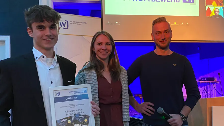 Schüler mit der Urkunde für den ersten Platz im Wettbewerb Wirtschaftswissen, dahinter ein Banner der Wirtschaftsjunioren Oberhavel.