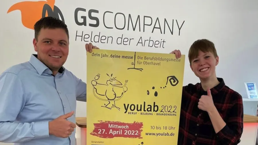 Zwei Personen halten das gelbe Plakat der Berufsbildungsmesse youlab 2022 für Oberhavel.